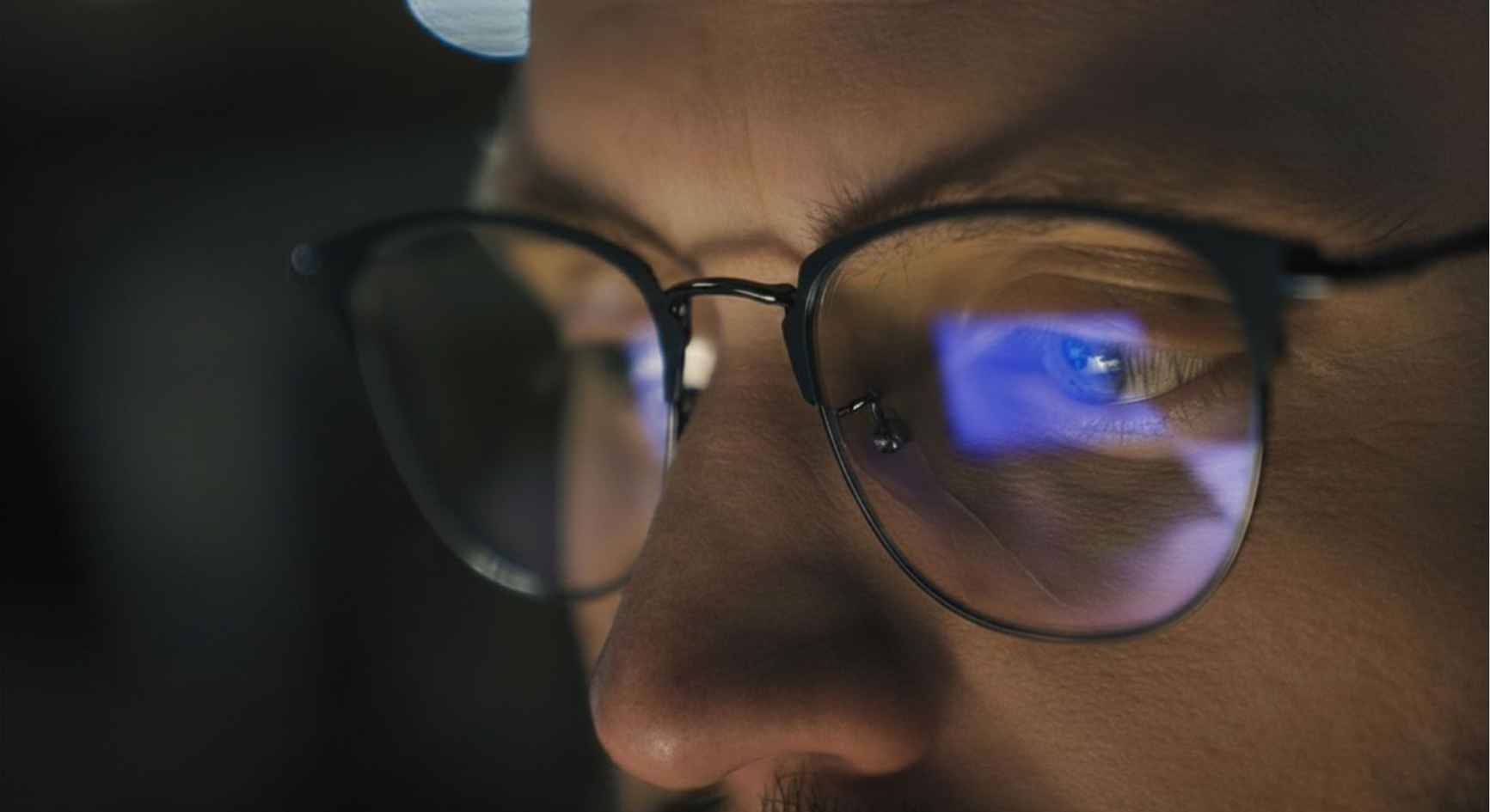 Close-up of a man's face with a screen reflected in his glasses at night
