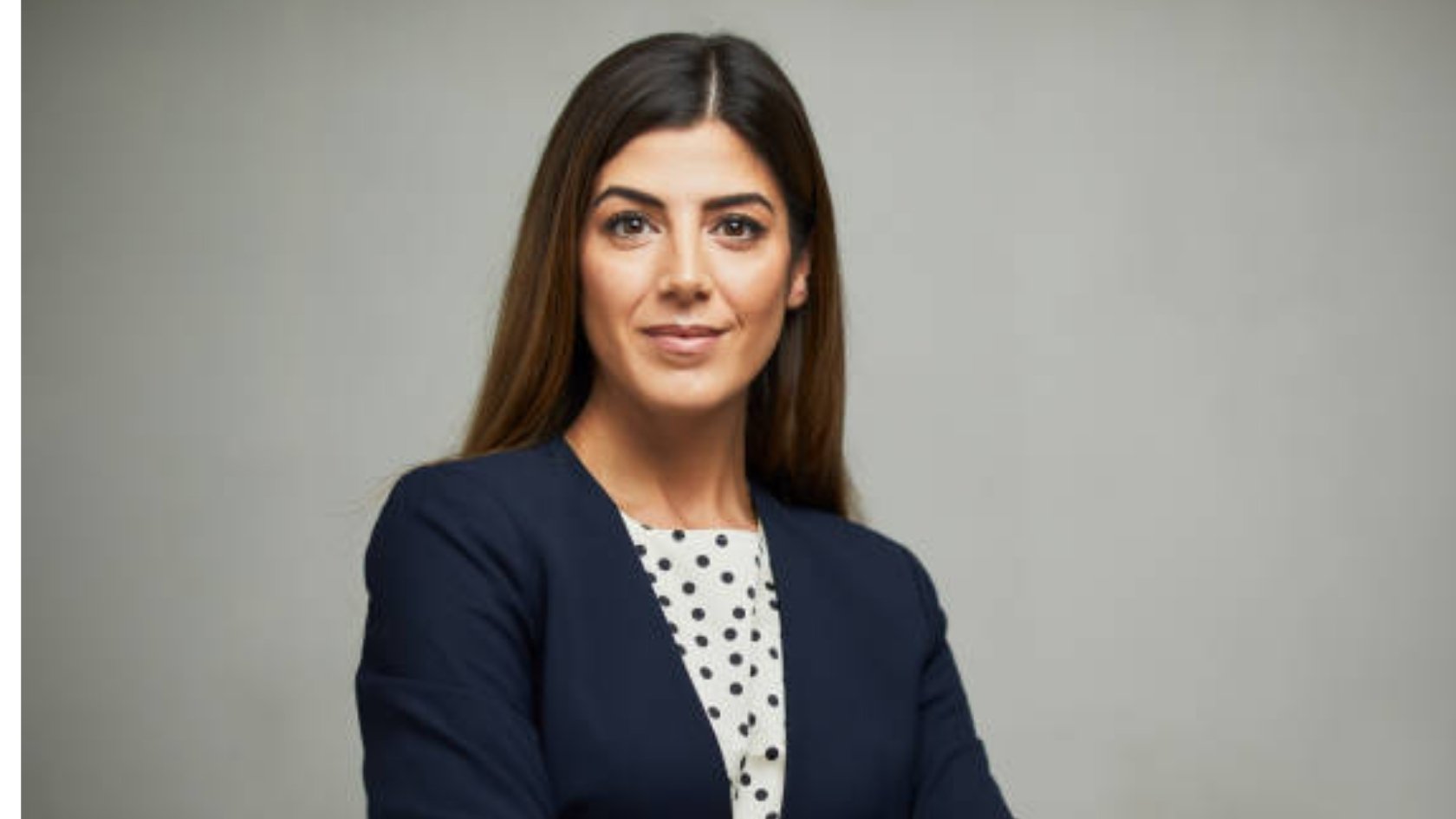 Confident professional woman in navy blazer with arms crossed against gray background