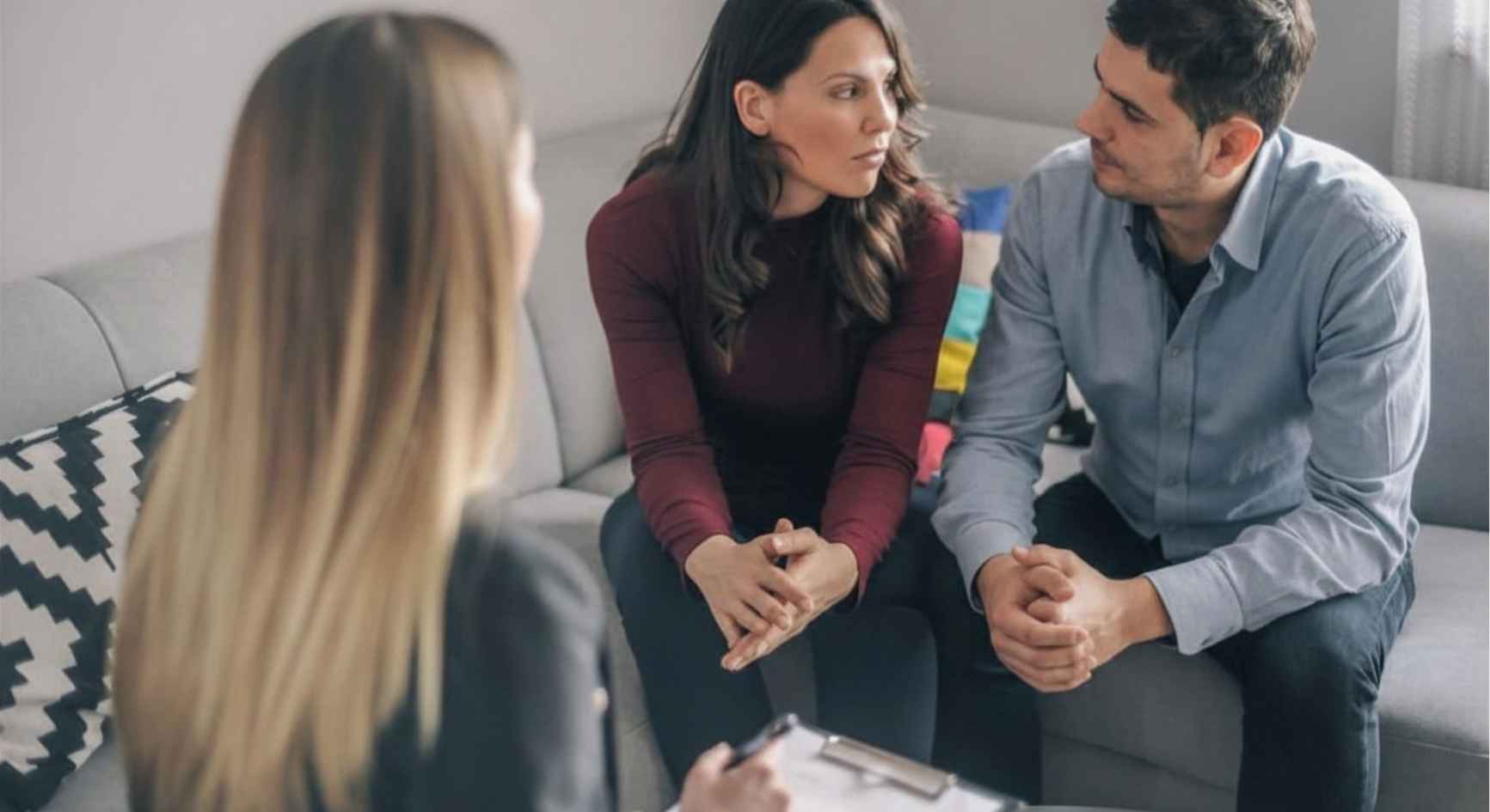 Couple exchanging a tense look during a counseling session with a female therapist