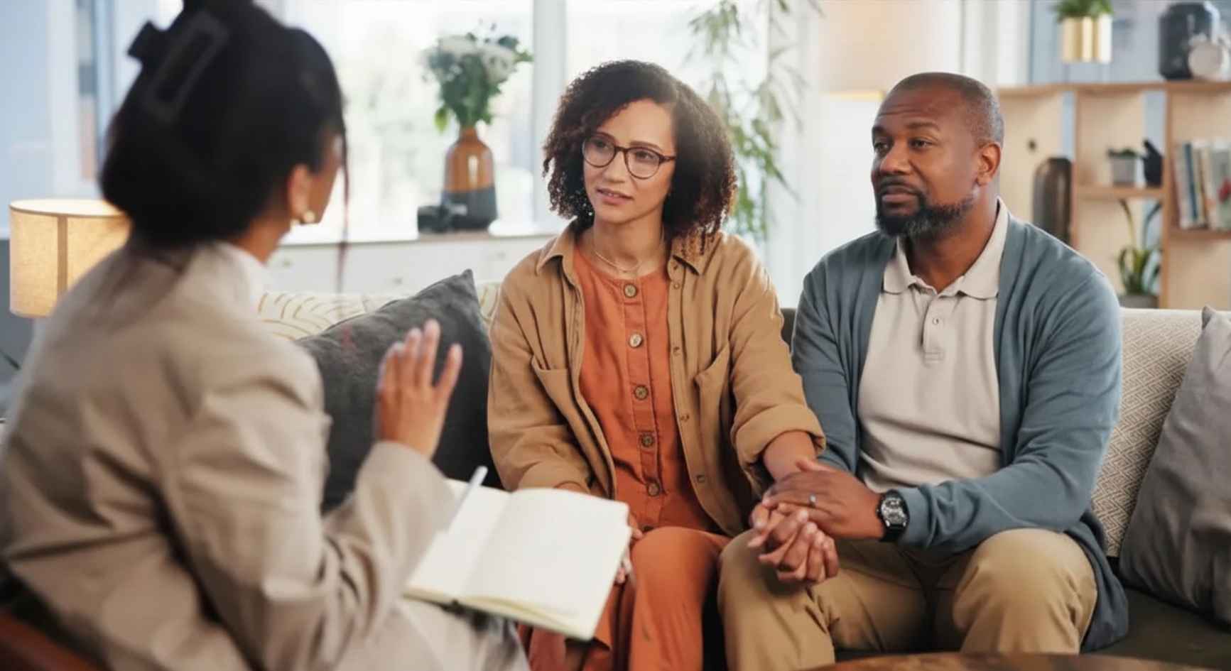 Couple holding hands while listening to a female therapist during a coaching session