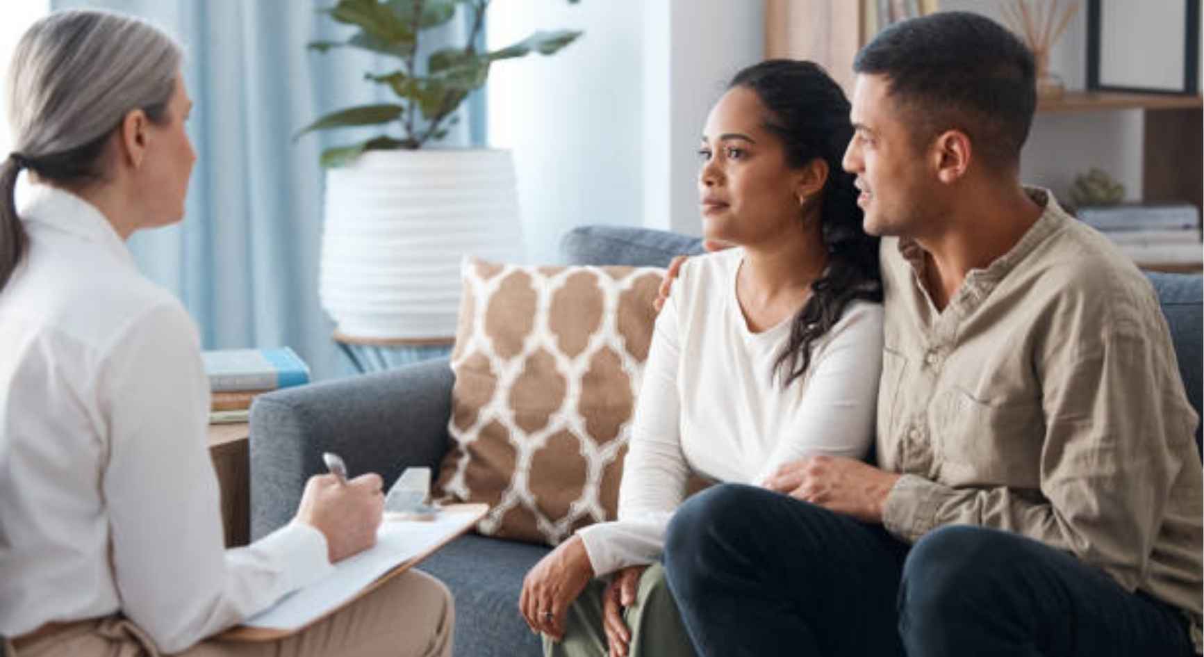 Couple sitting together on a couch listening to a female therapist taking notes