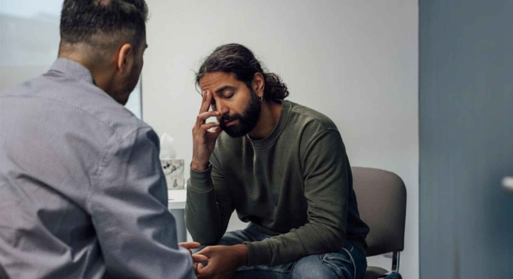 Distressed man in coaching session with male therapist in clinical office