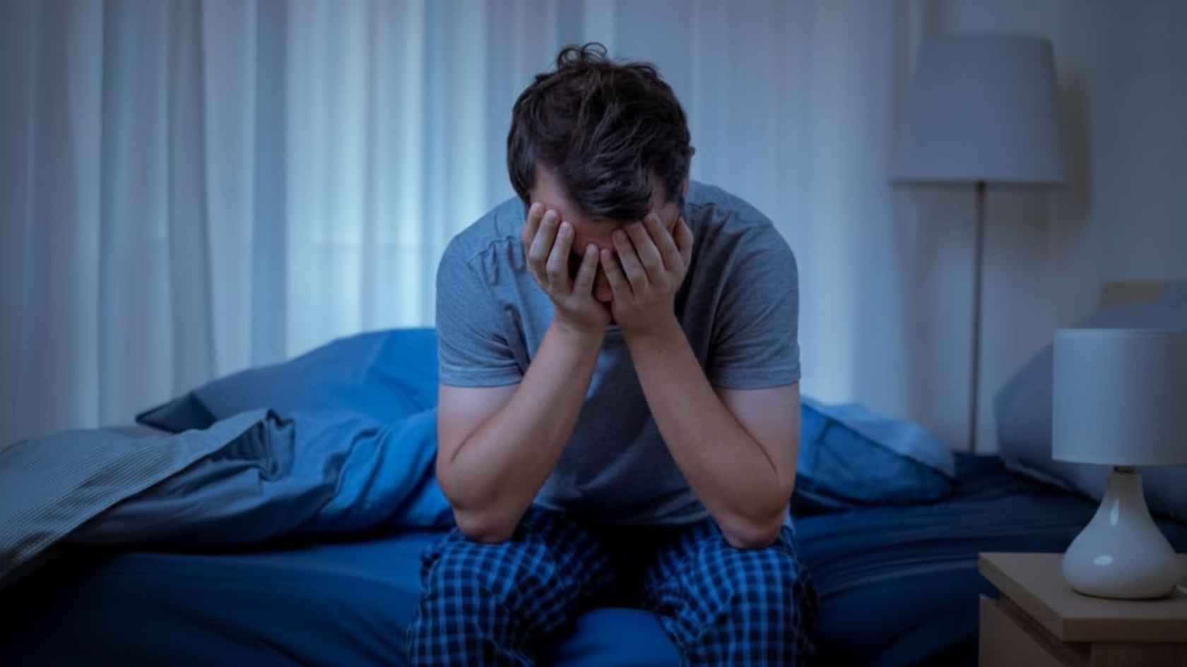 Distressed man sitting on the edge of a bed with his face in his hands at night
