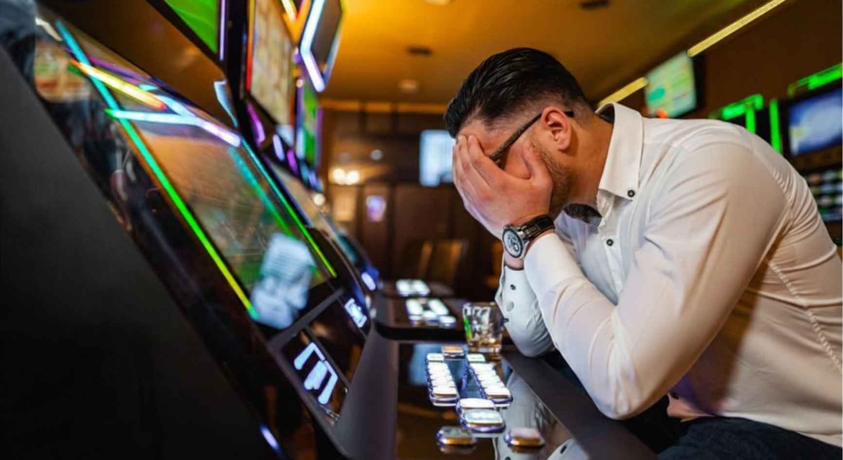 Distressed man with head in hands at a slot machine seeking help from gambling addiction therapists