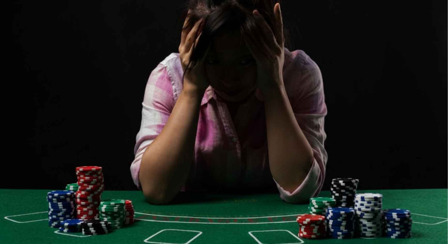 Distressed woman holding her head at a poker table surrounded by stacks of chips