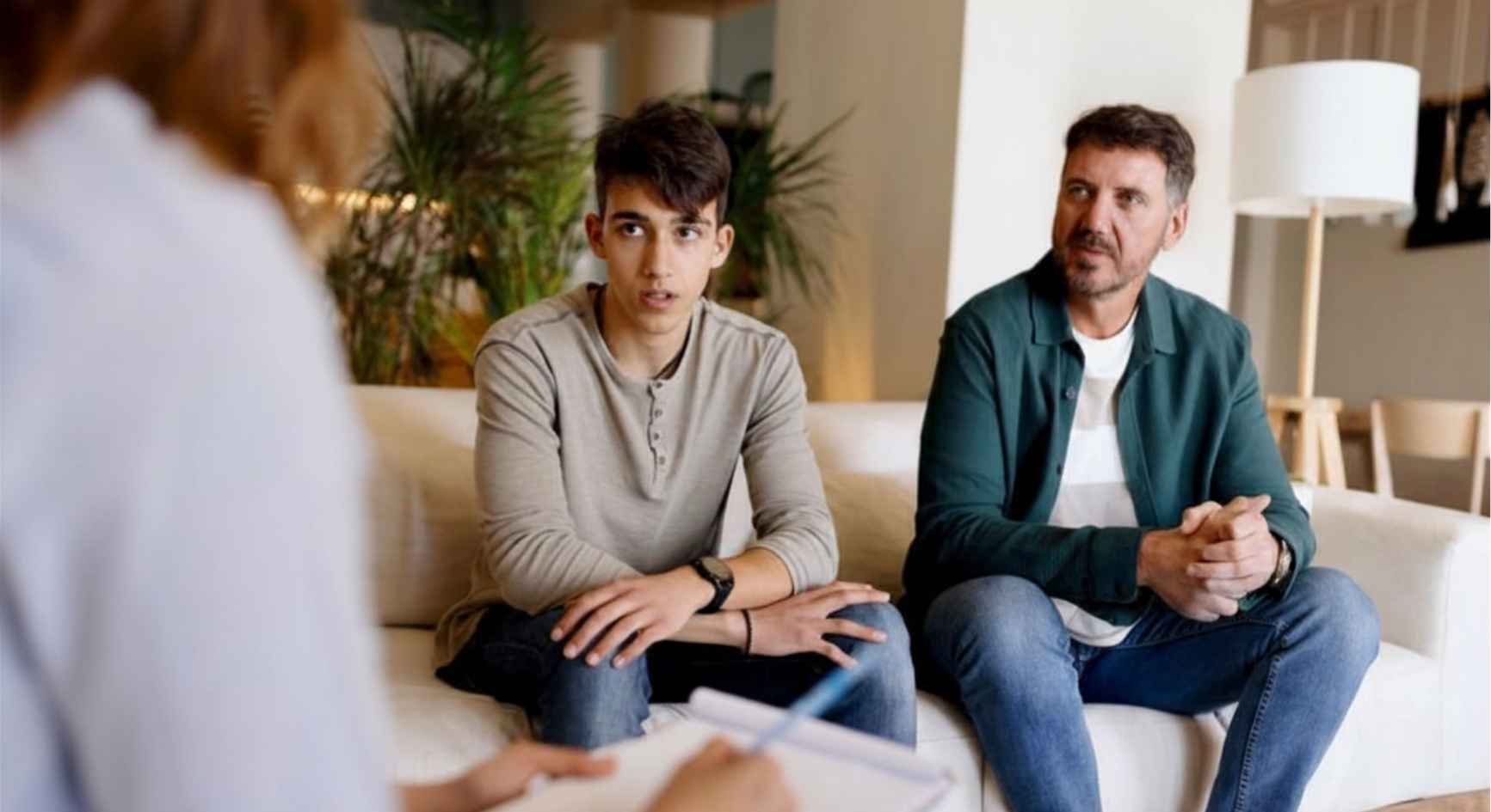 Father and teenage son speaking with a female therapist during a family counseling session