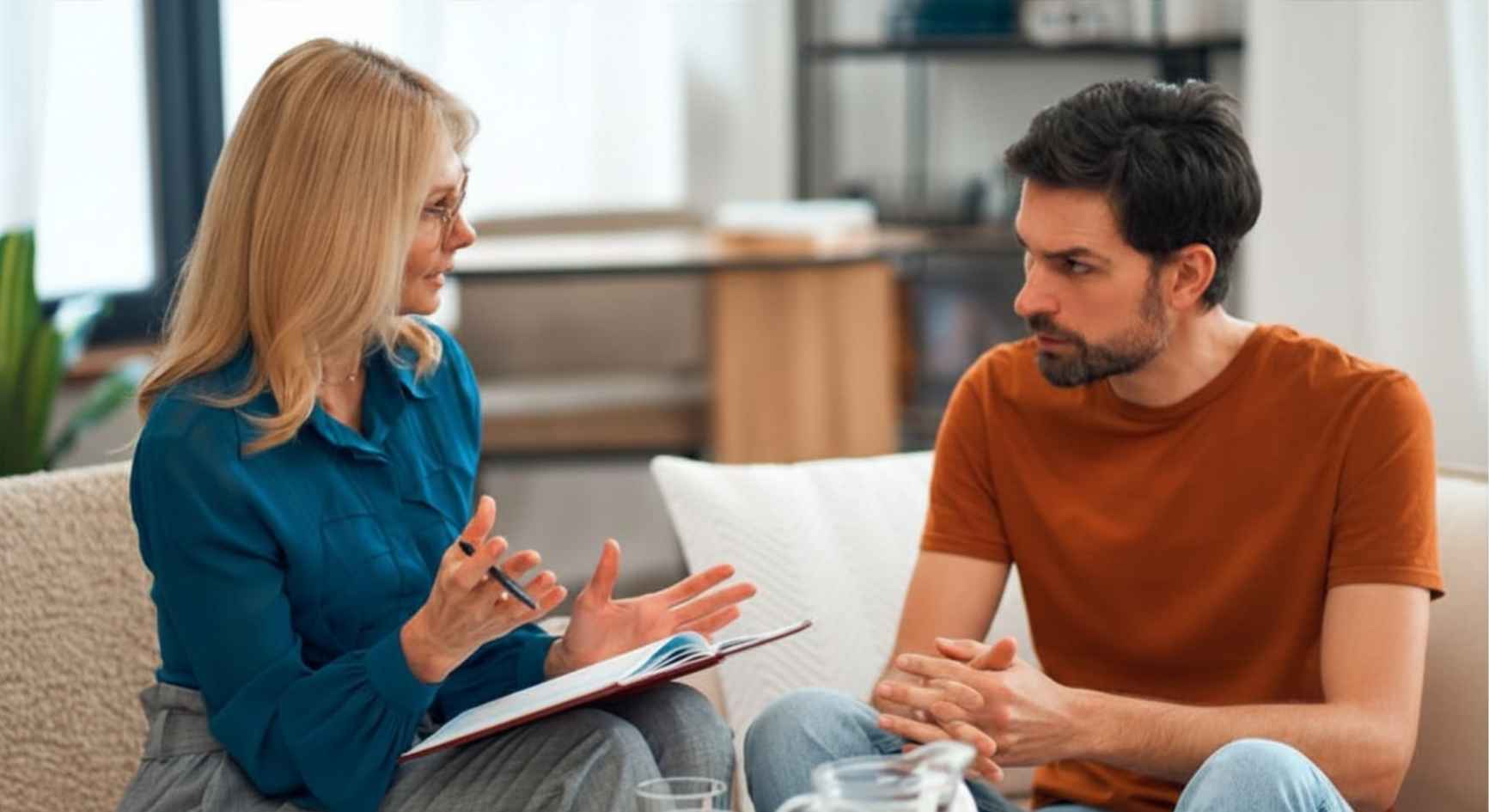 Female therapist with notebook speaking to a male client during a counseling session