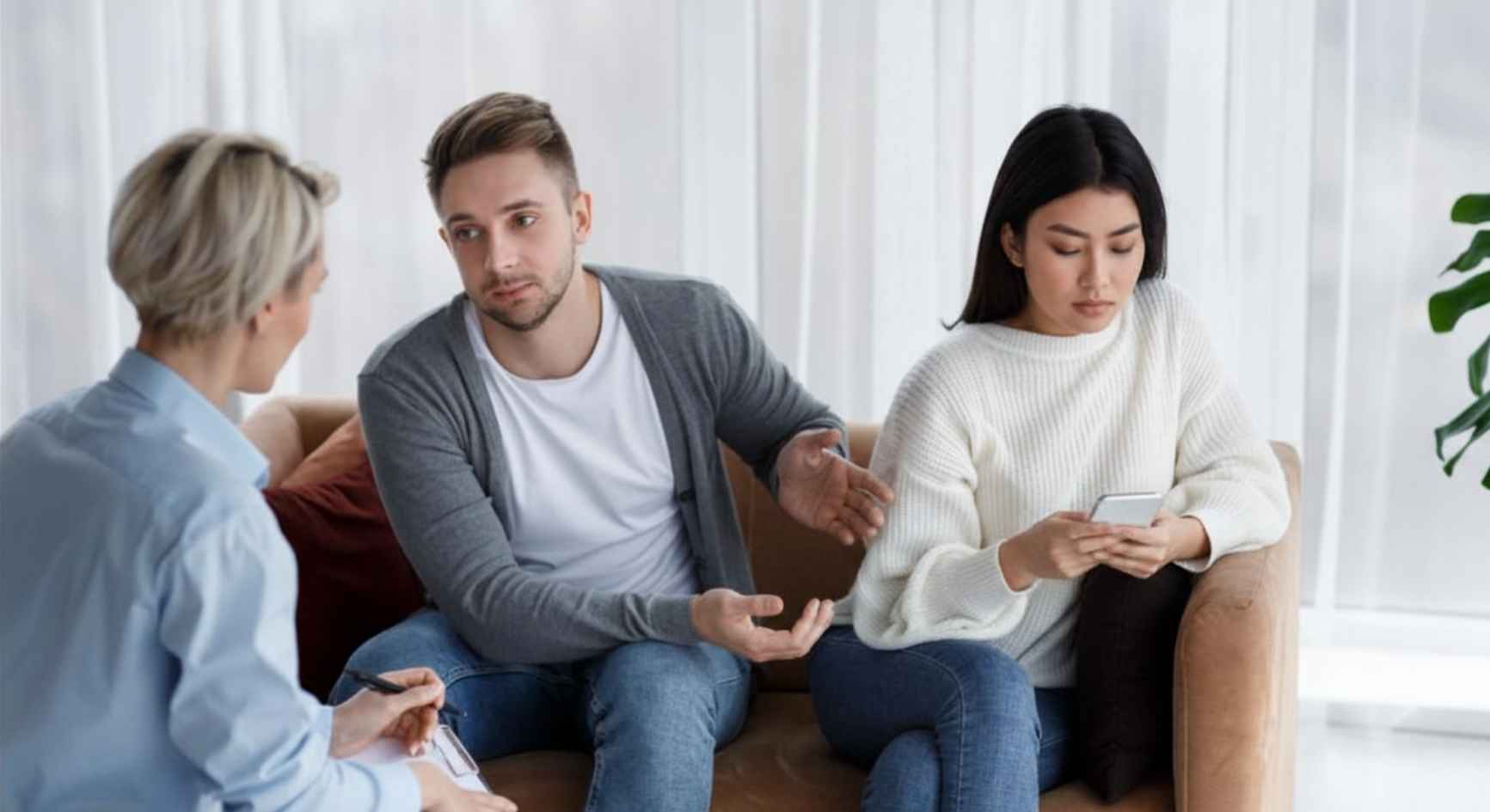 Frustrated man talking to a therapist while his partner looks at her phone during couples coaching