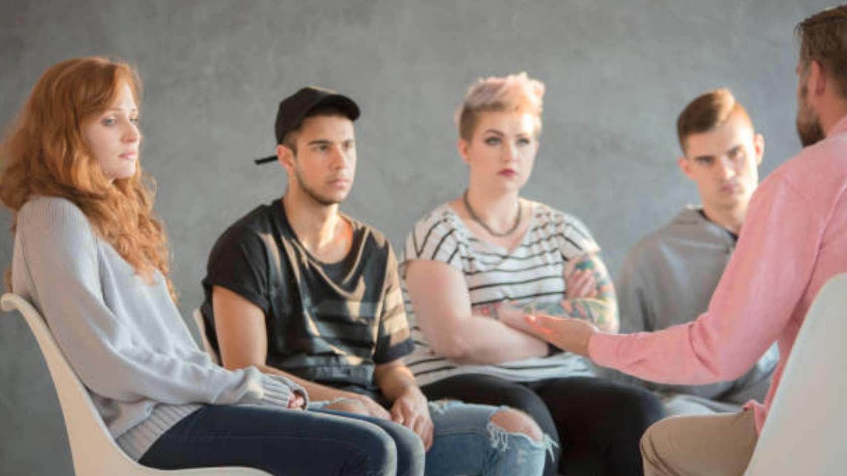 Group of young adults listening attentively to a counselor during a therapy session
