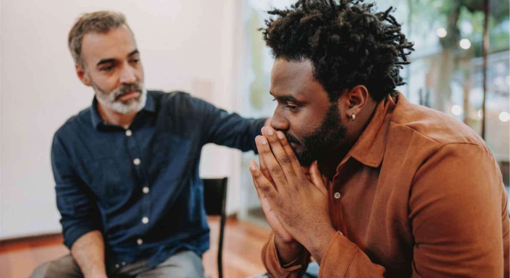 Man comforting distressed friend with hand on shoulder during support group