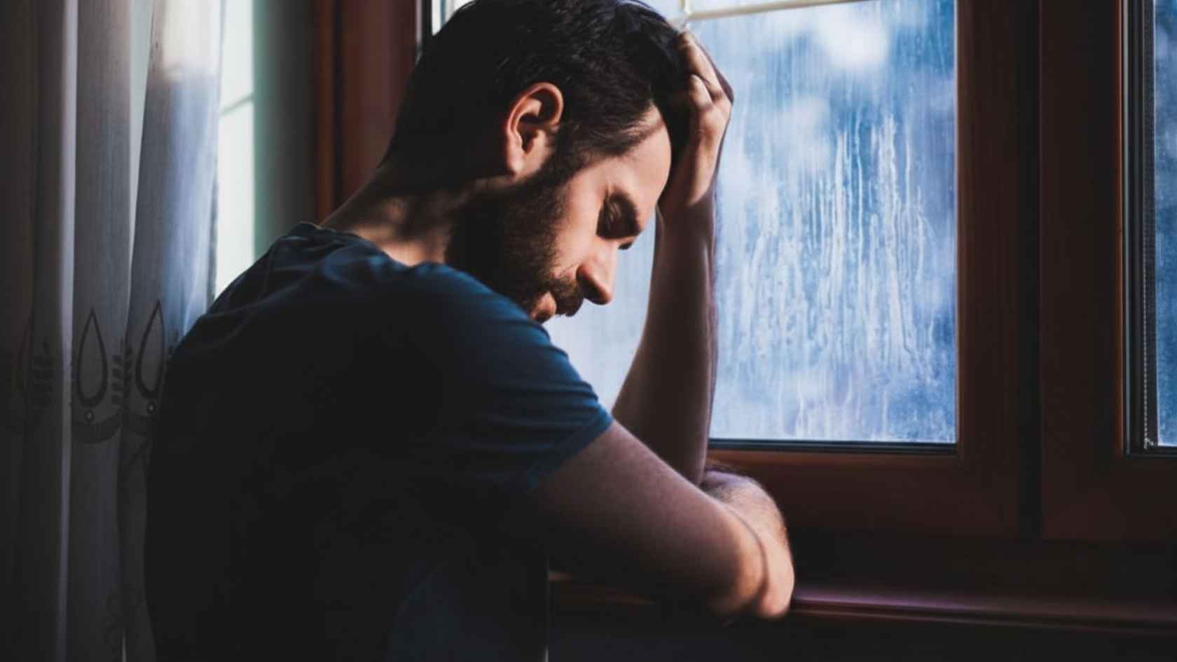 Man leaning against rainy window with head down looking sorrowful
