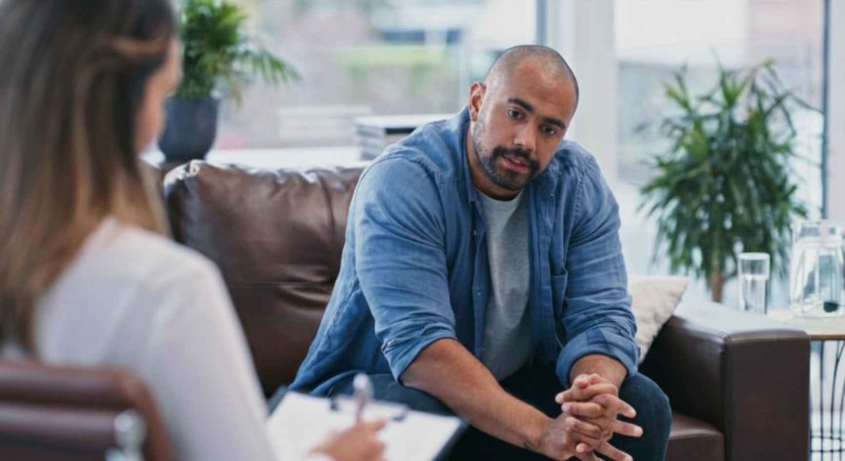 Man sitting on a couch speaking to a female therapist taking notes during a coaching session