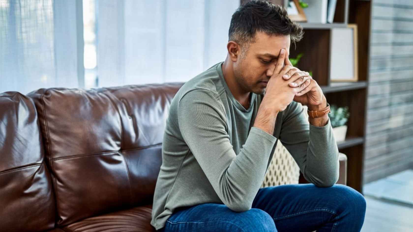 Man sitting on leather couch with head in hands looking distressed