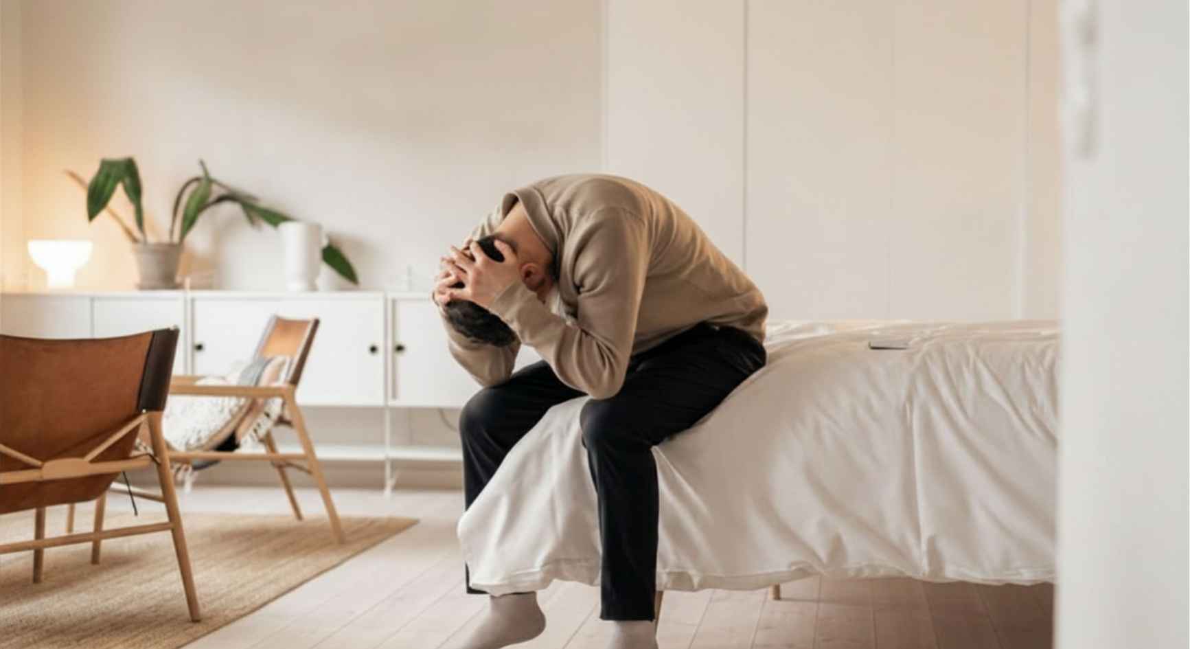 Man sitting on the edge of a bed with his head in his hands