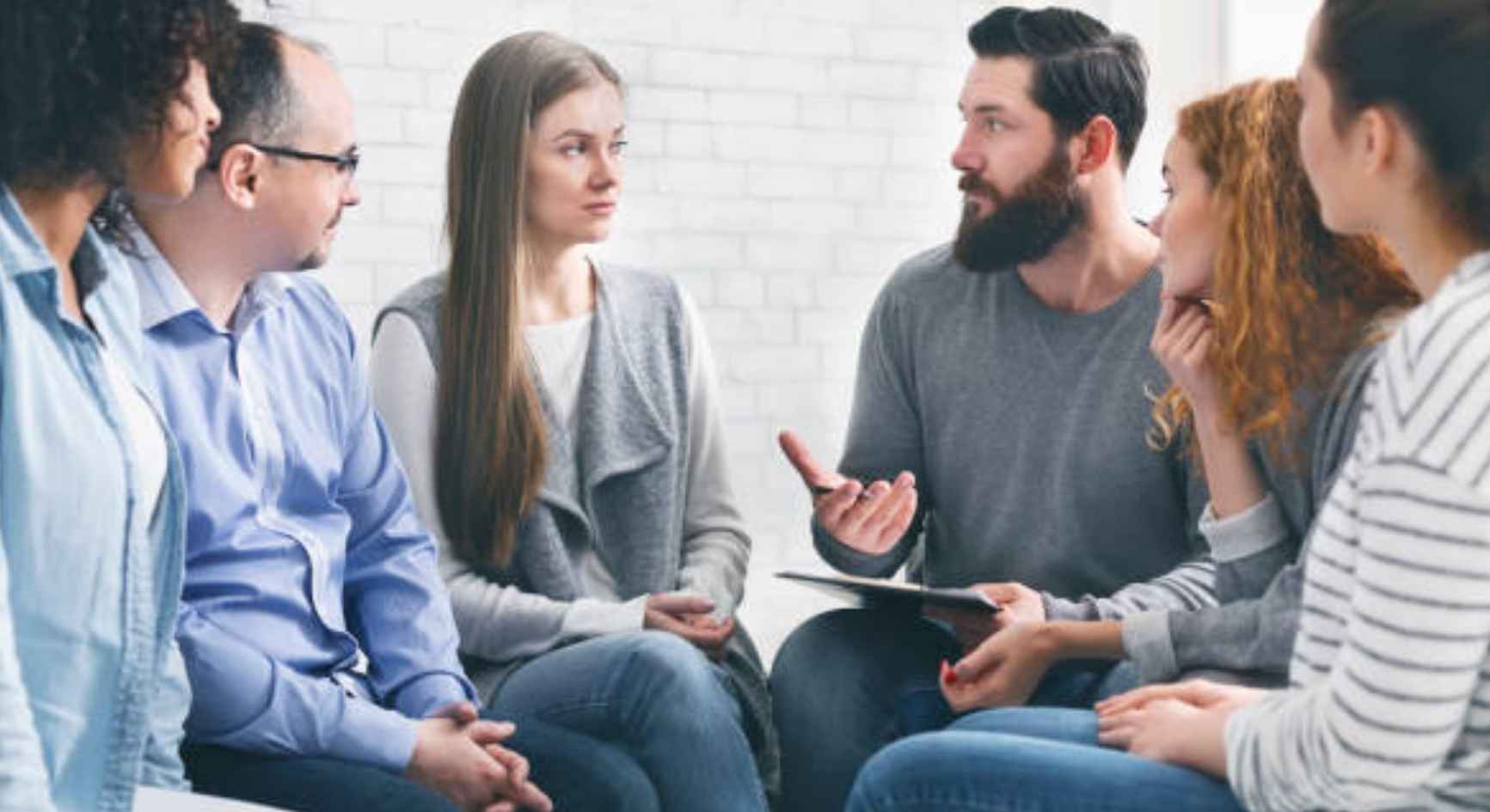 Man speaking to a diverse group of people seated in a circle during a support meeting