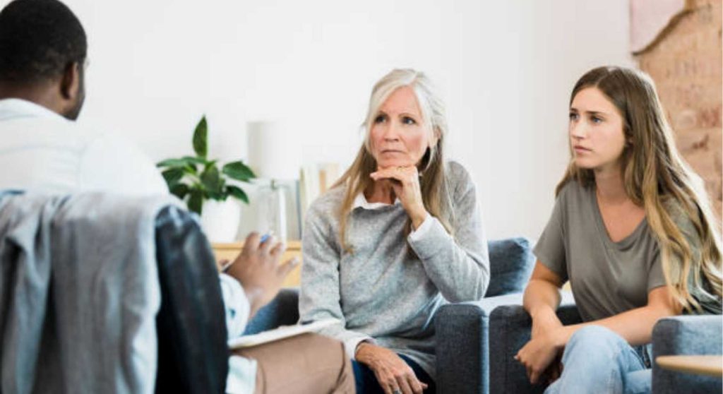 Mother and adult daughter listening to a male therapist during a family counseling session