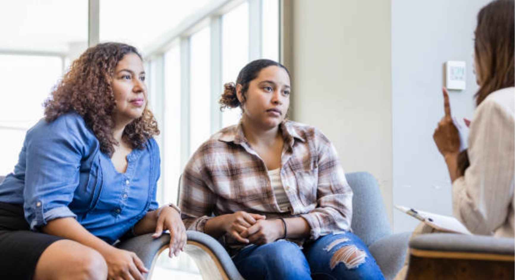Mother and teenage daughter listening to a female therapist during a counseling session