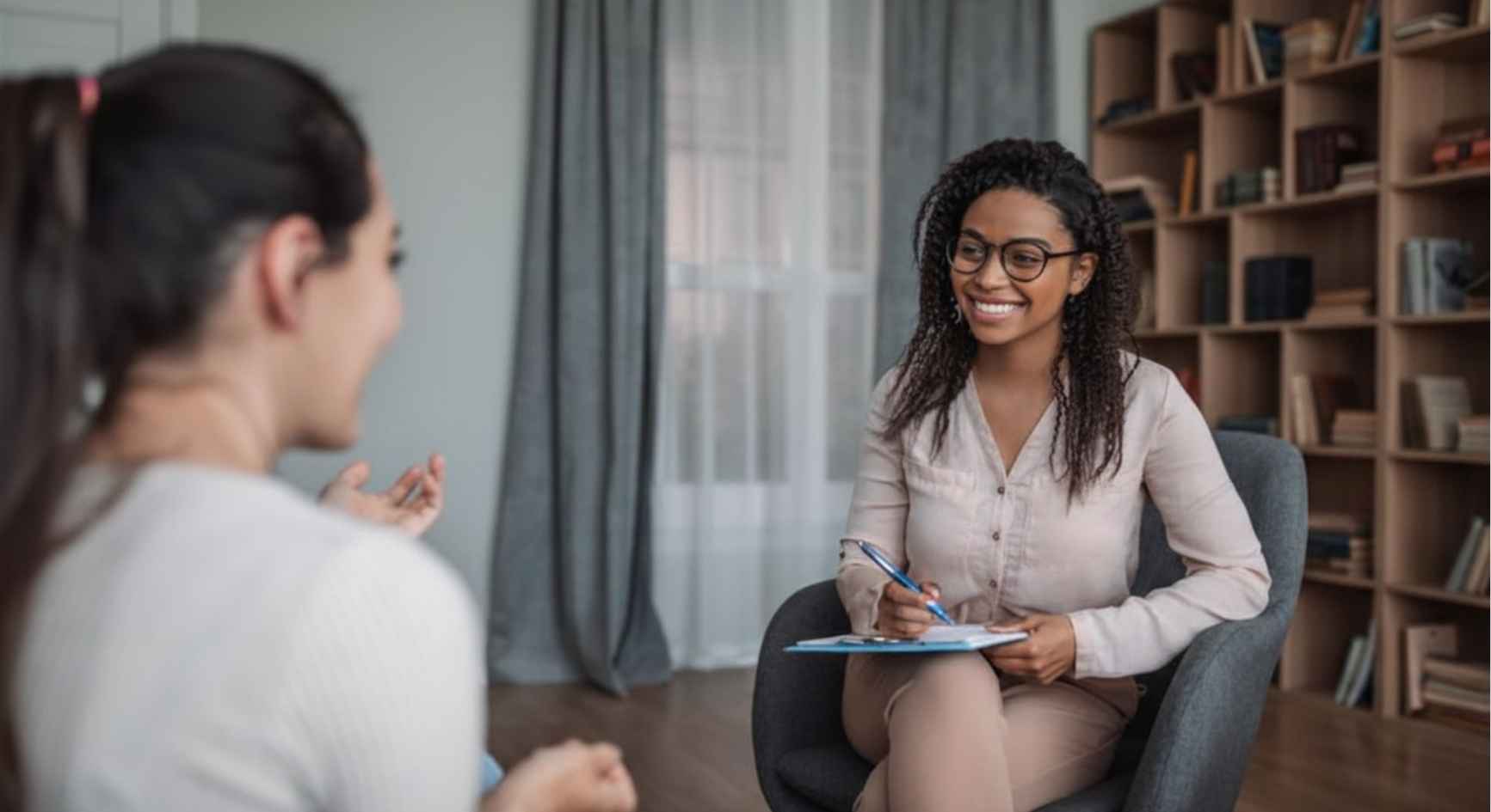 Smiling female therapist with clipboard listening to client in office