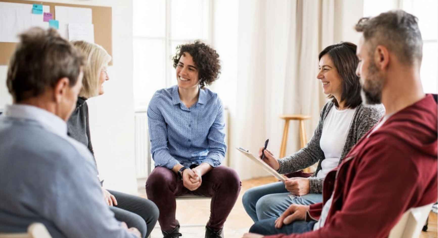Smiling group of people of different ages seated in a circle during a therapy session