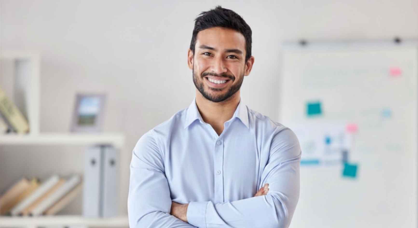 Smiling male counselor with arms crossed standing in a therapy office