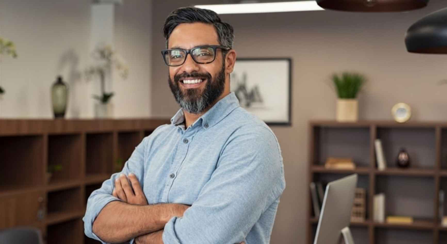 Smiling man with glasses and arms crossed standing in a modern office