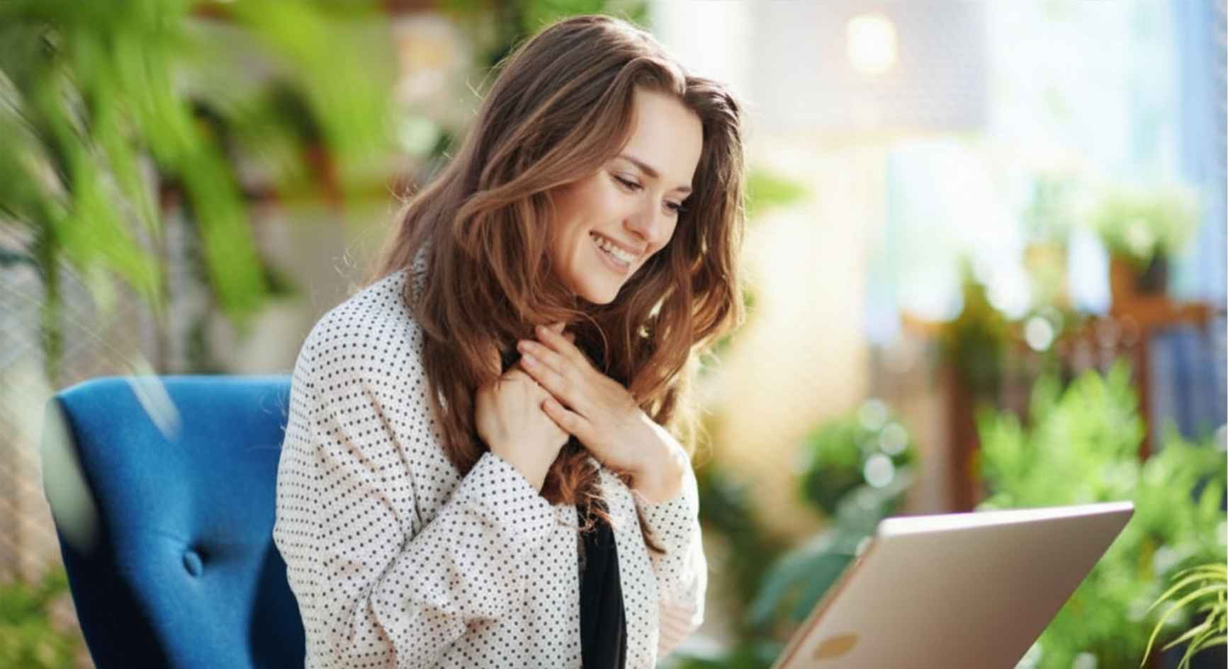 Smiling woman on laptop during online therapy session in sunlit garden room