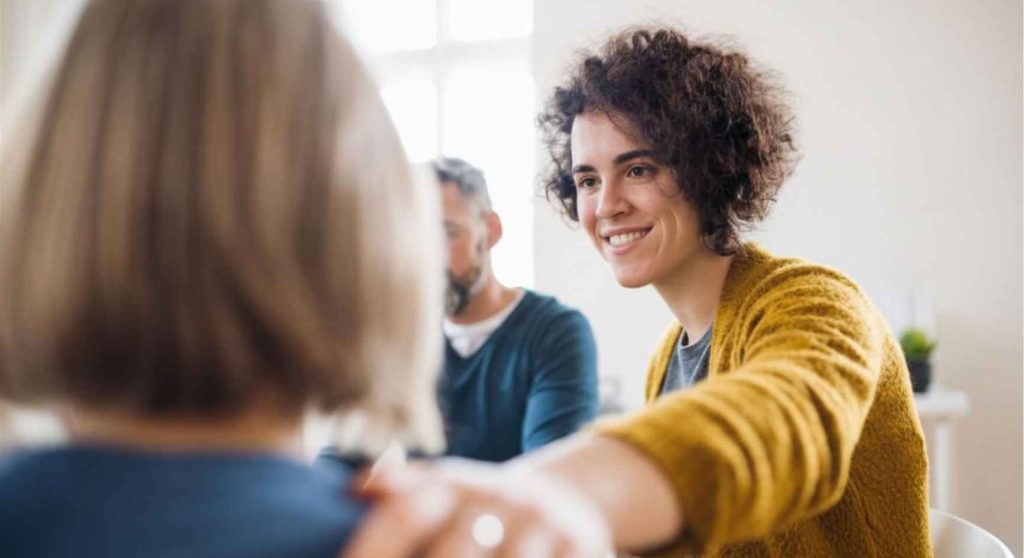 Smiling woman placing a reassuring hand on another person's shoulder during a support group