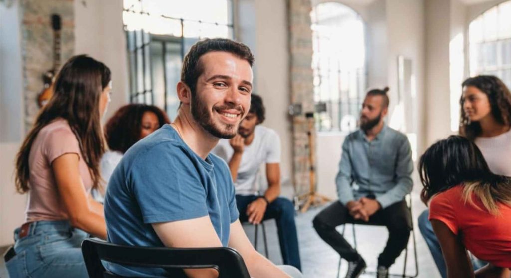 Smiling young man seated with a diverse group during a support meeting