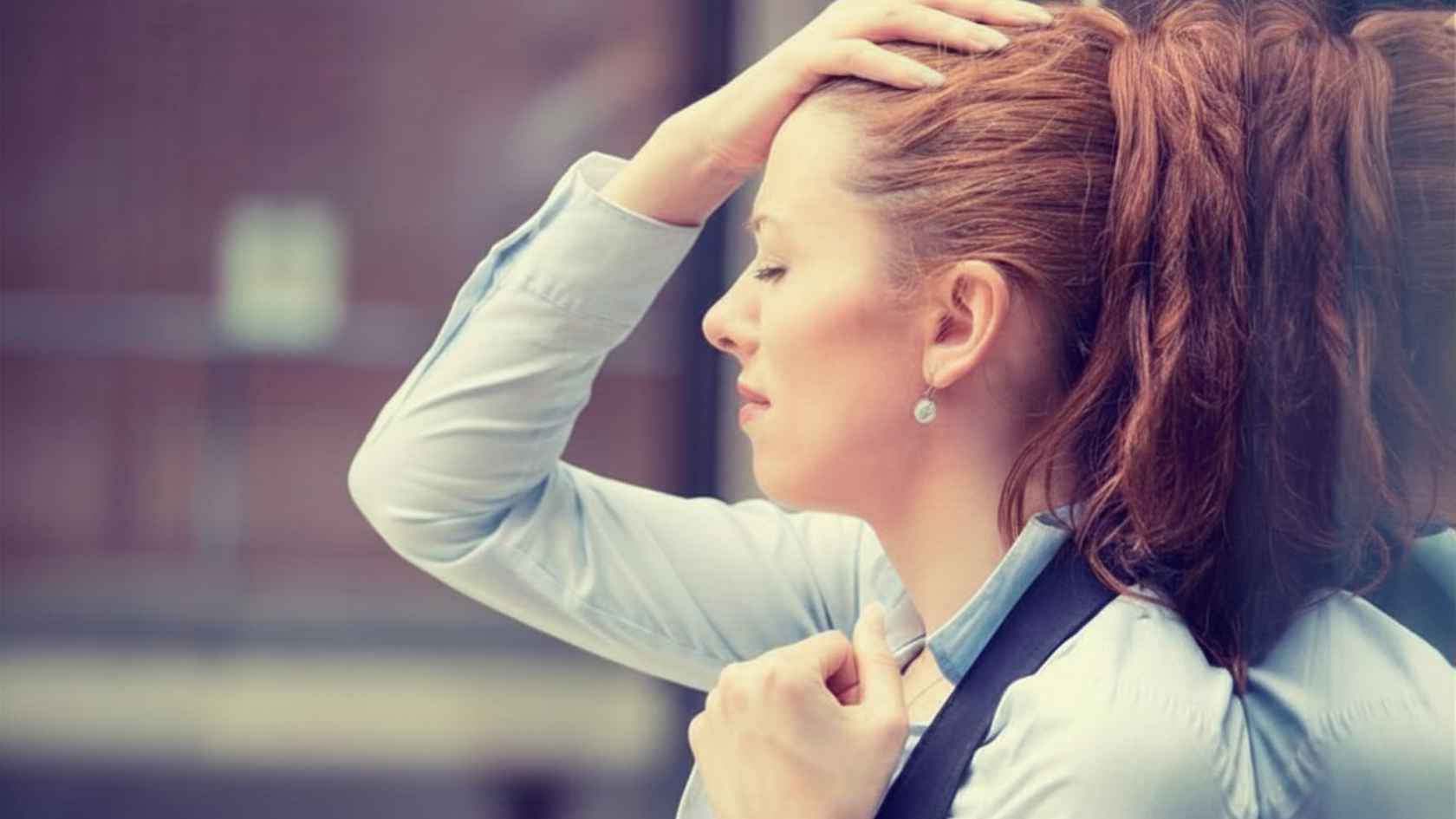 Stressed woman with her hand on her head standing outside a building