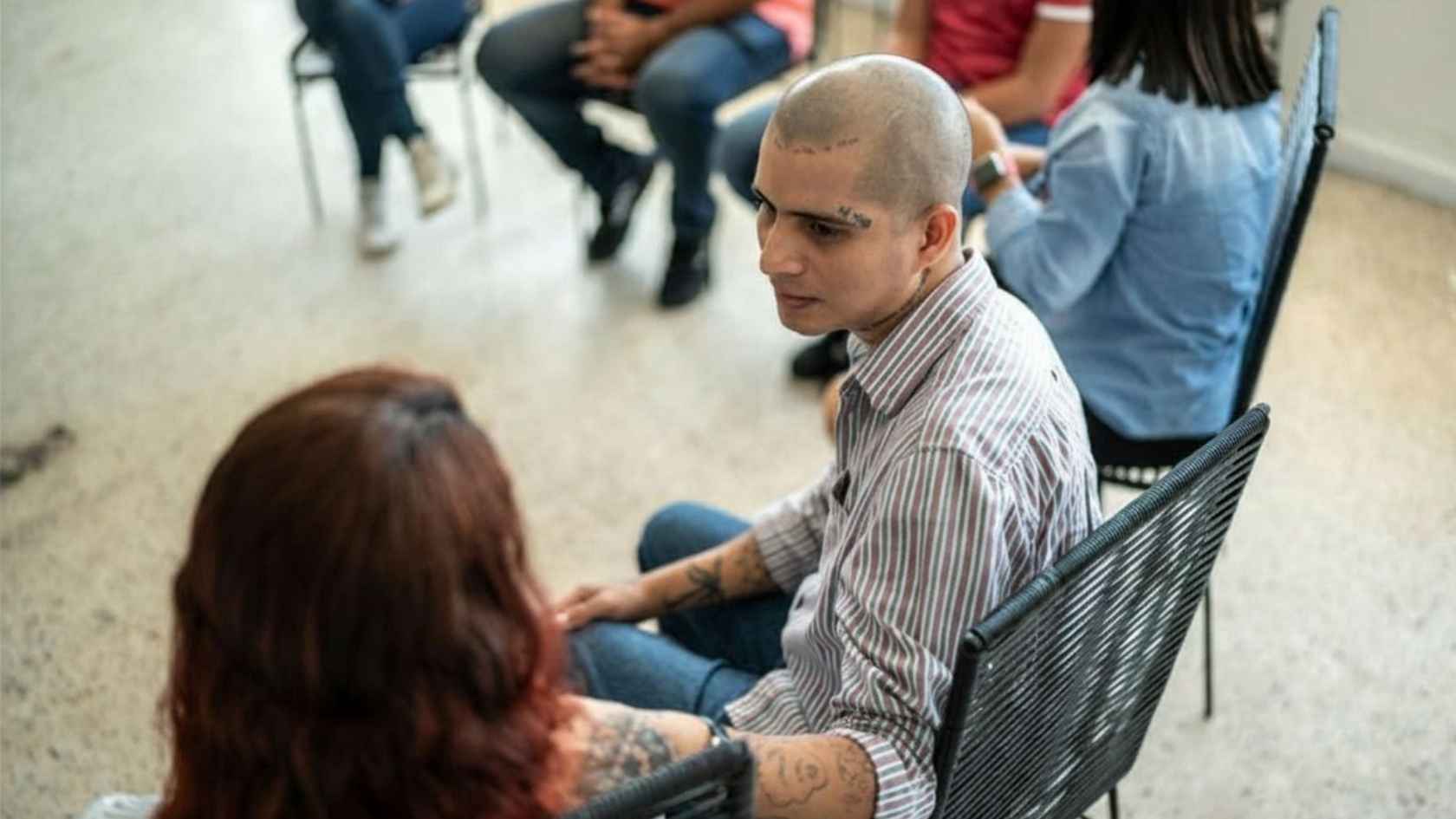 Tattooed man speaking quietly with a woman during a group support meeting