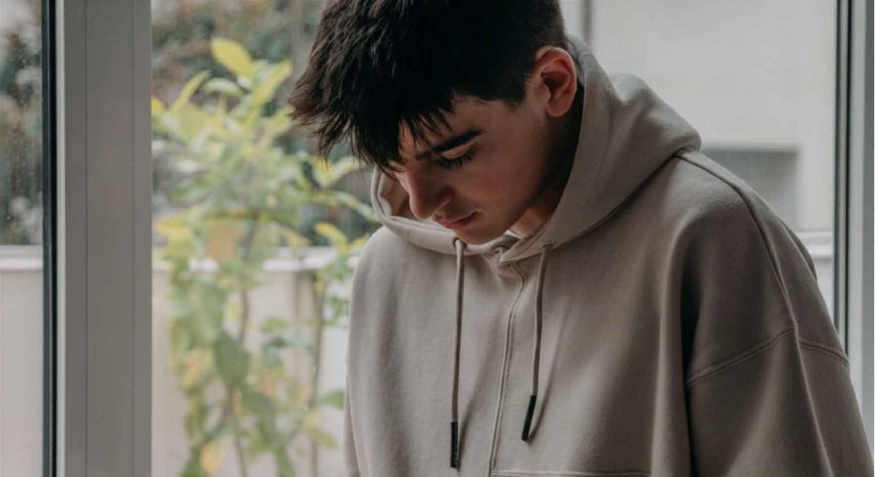Teenage boy in a hoodie focused on his phone by a window