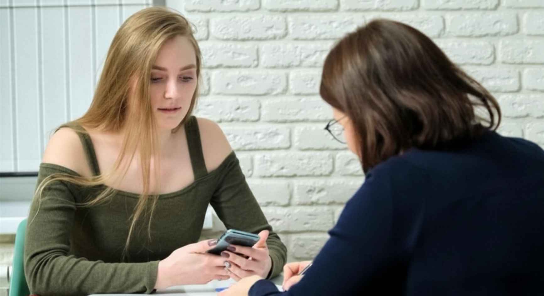 Teenage girl showing her phone to a female counselor during a therapy session