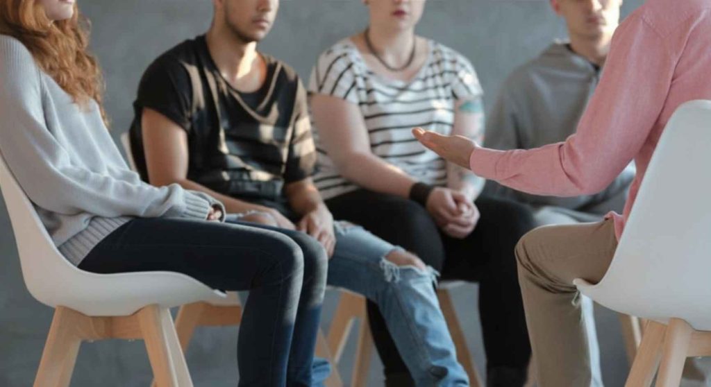 Therapist gesturing toward a group of young adults seated during a counseling session