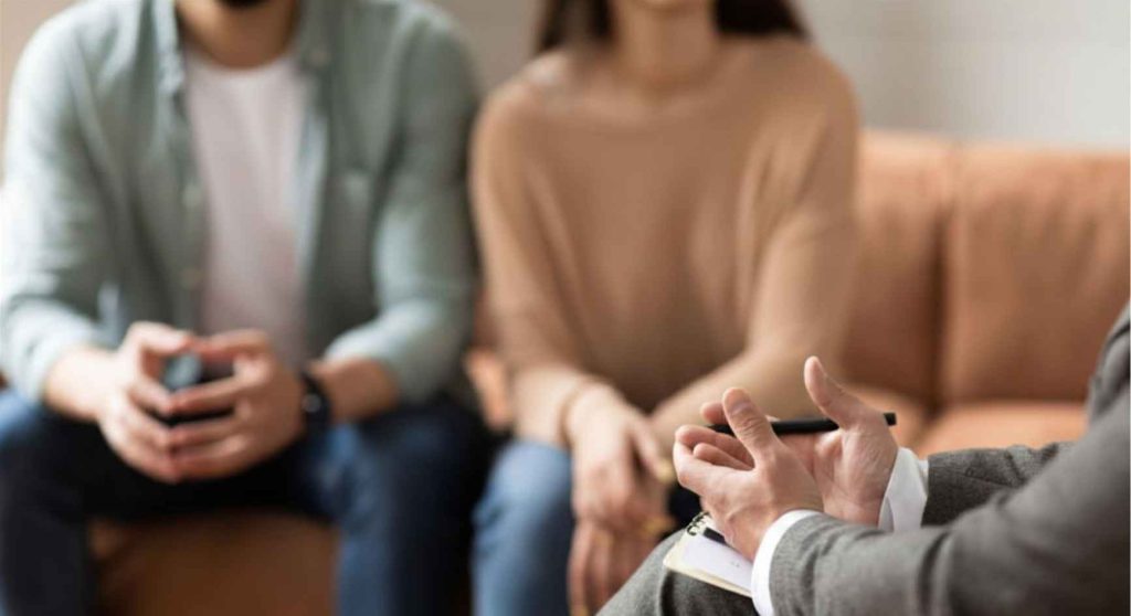 Therapist with notepad speaking to a couple during a coaching session