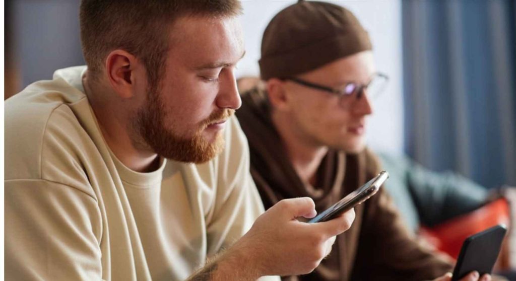 Two young men focused on their phones while sitting side by side