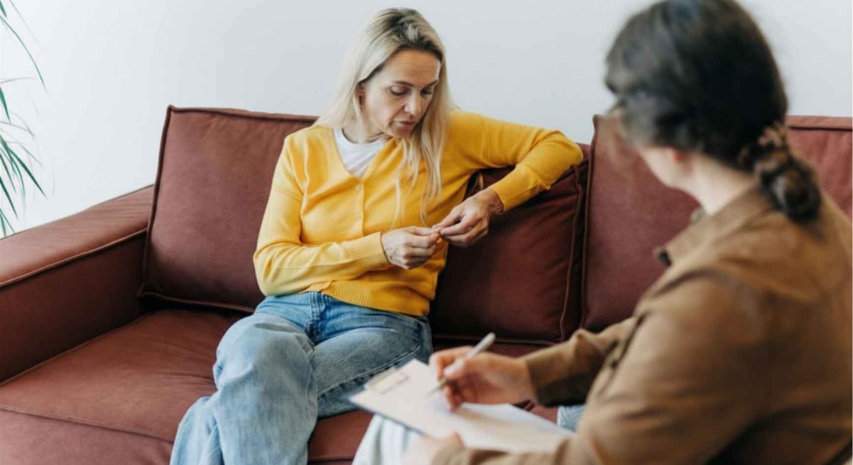 Woman in a yellow cardigan looking down thoughtfully as a therapist takes notes