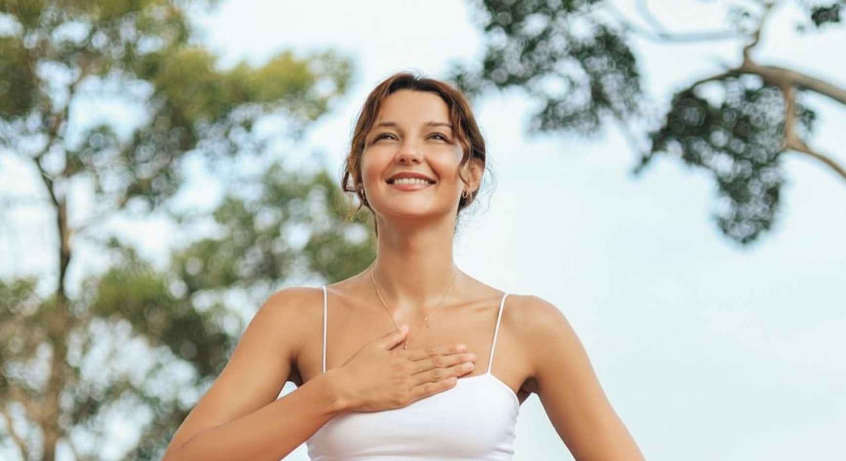 Woman smiling outdoors with hand on chest feeling calm and hopeful