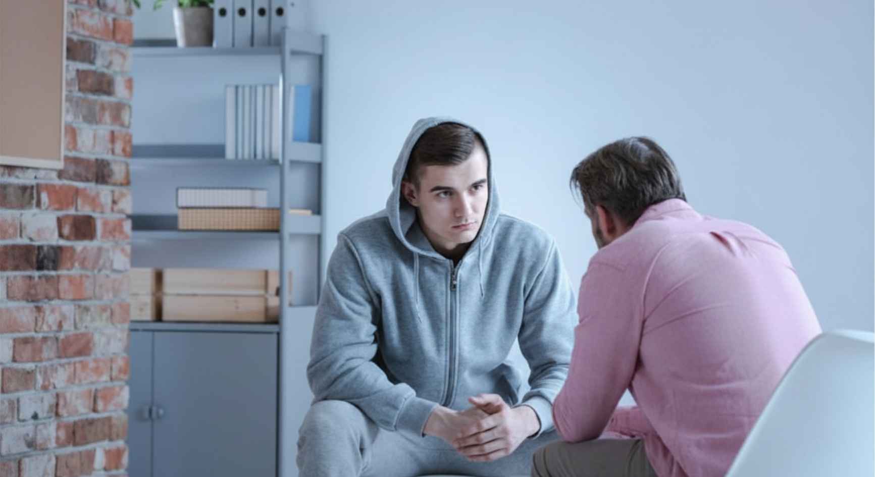 Young man in a hoodie listening to a counselor during a one-on-one therapy session