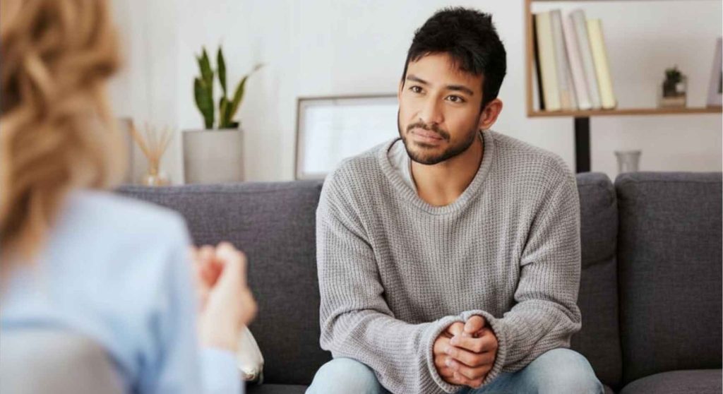Young man sitting on a couch listening attentively to a female therapist during a session