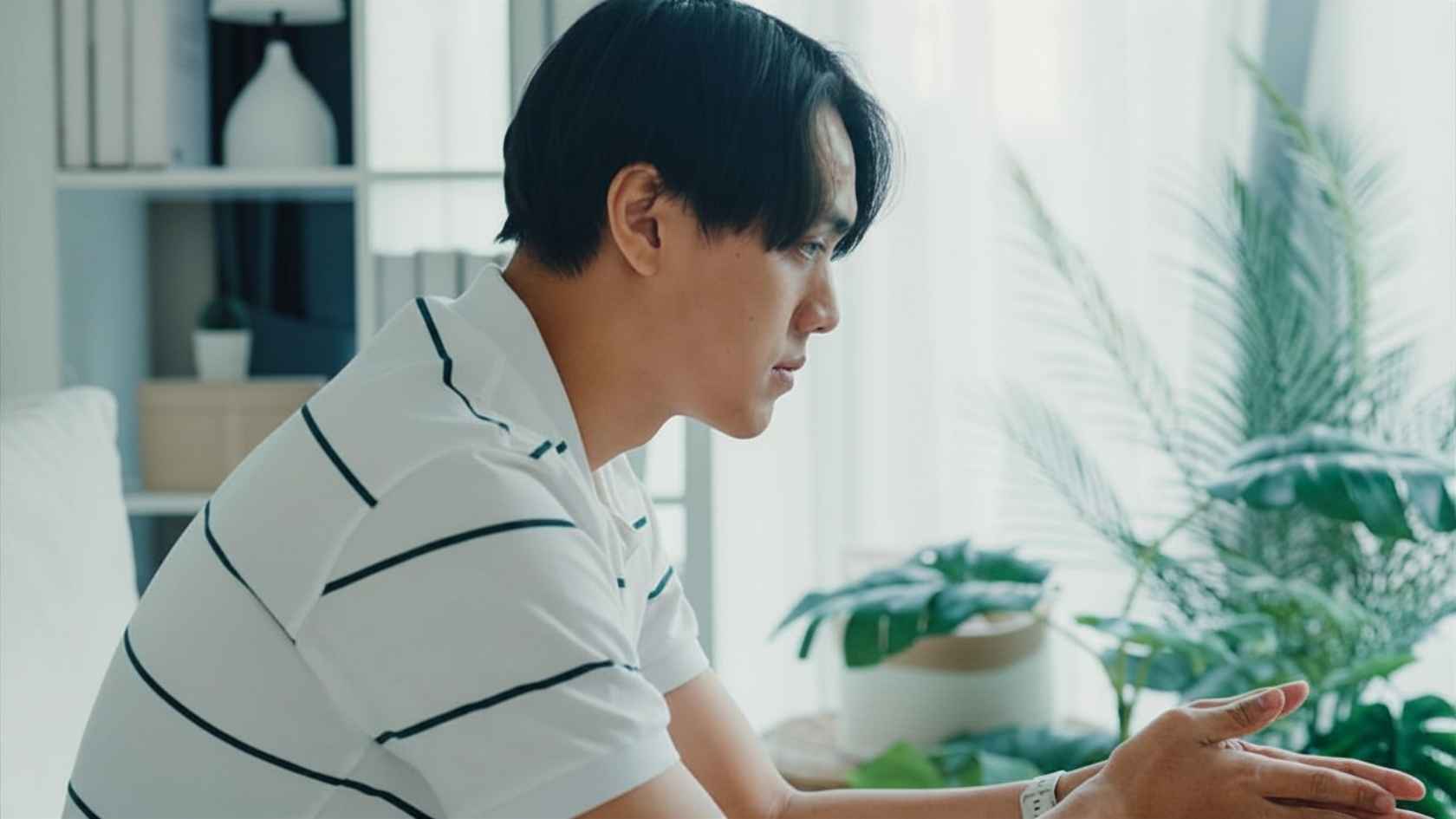 Young man speaking thoughtfully while seated in a bright living room