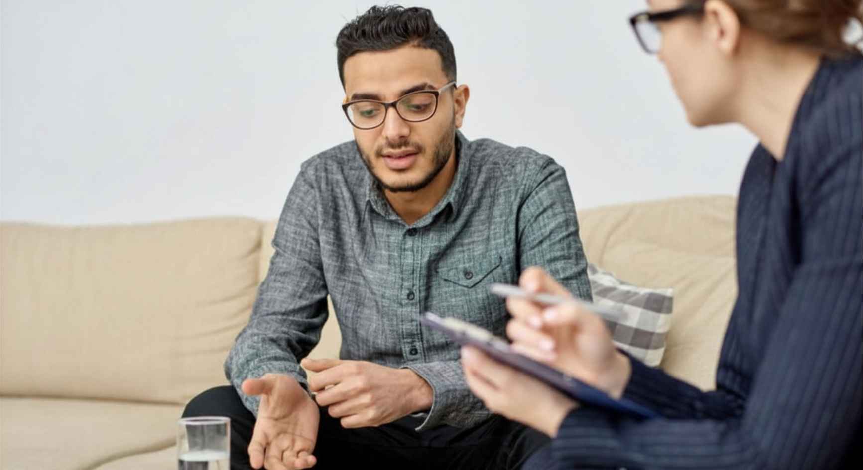 Young man speaking to a female therapist with a clipboard during a coaching session