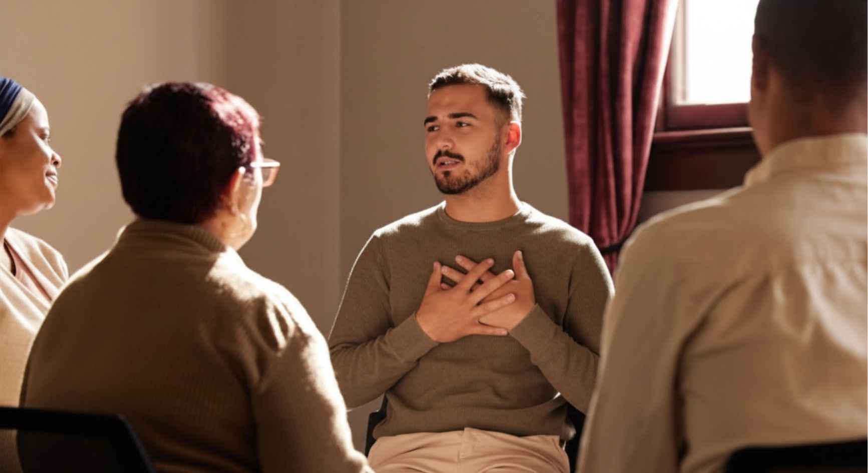 Young man with hands on his chest sharing openly during a group therapy session.