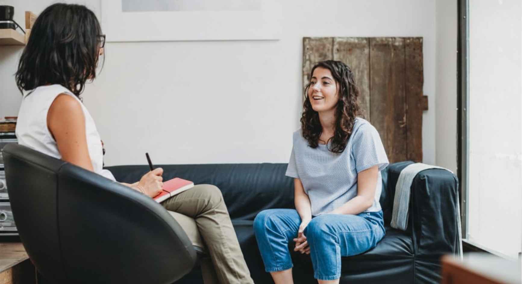 Young woman smiling during therapy session with counselor taking notes