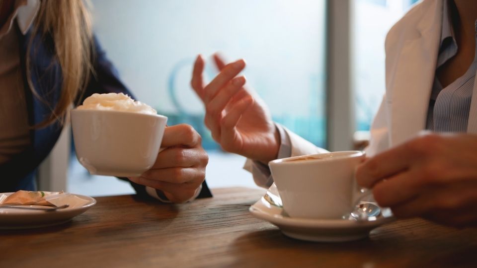 What Does a Mental Health Coach Do hero image of a coach and a client meeting over coffee.